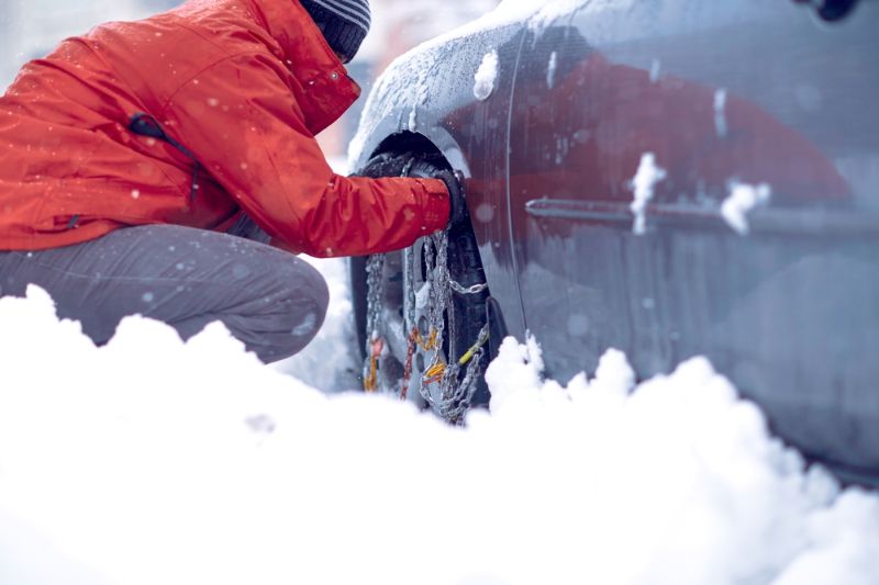 Man applies snow chains to car tyre